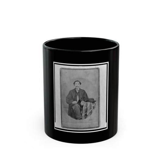 Black and white studio portrait of a seated man in a dark suit, a bowler hat resting on a patterned cloth beside him.