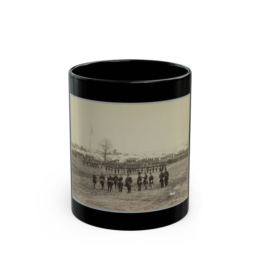 Sepia print showing officers on an open field before ranks of soldiers and rows of white tents, with a flag.