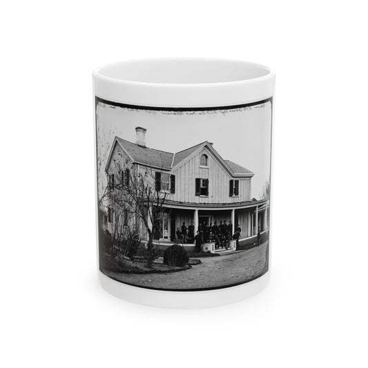 Black and white view of uniformed men posed on the porch of a two-story wooden house with bare trees.