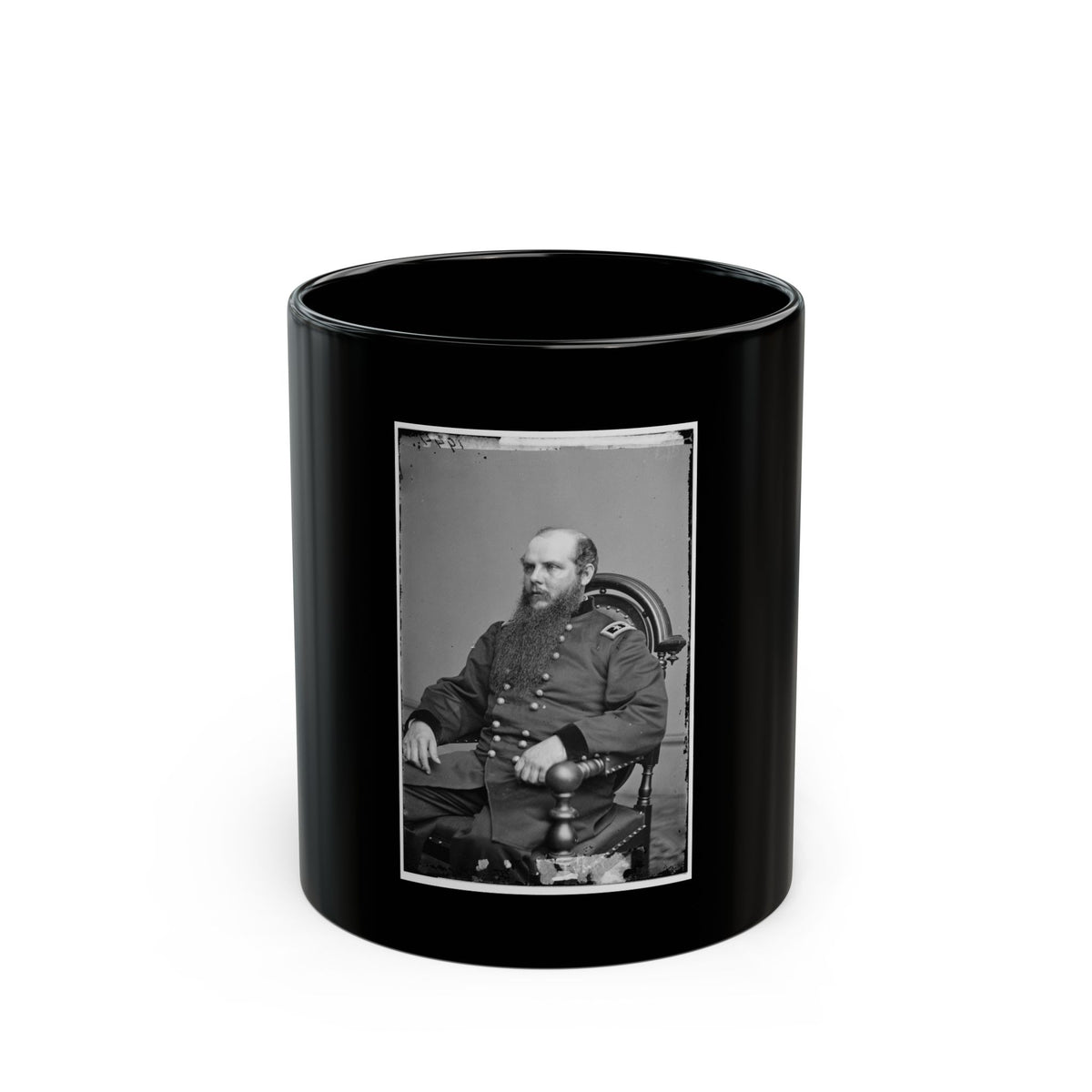 Black and white vintage portrait of a long-bearded man in a military coat seated in a carved wooden armchair.