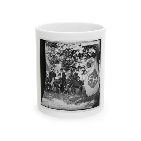Black and white view of six men posed beneath a tree beside a large flag bearing a white anchor.
