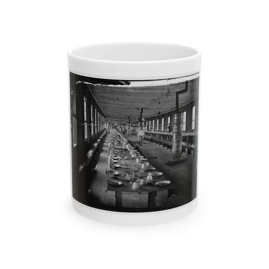 Black and white historical view of a long wooden mess hall, with tables set for a meal and a large ornate stove.