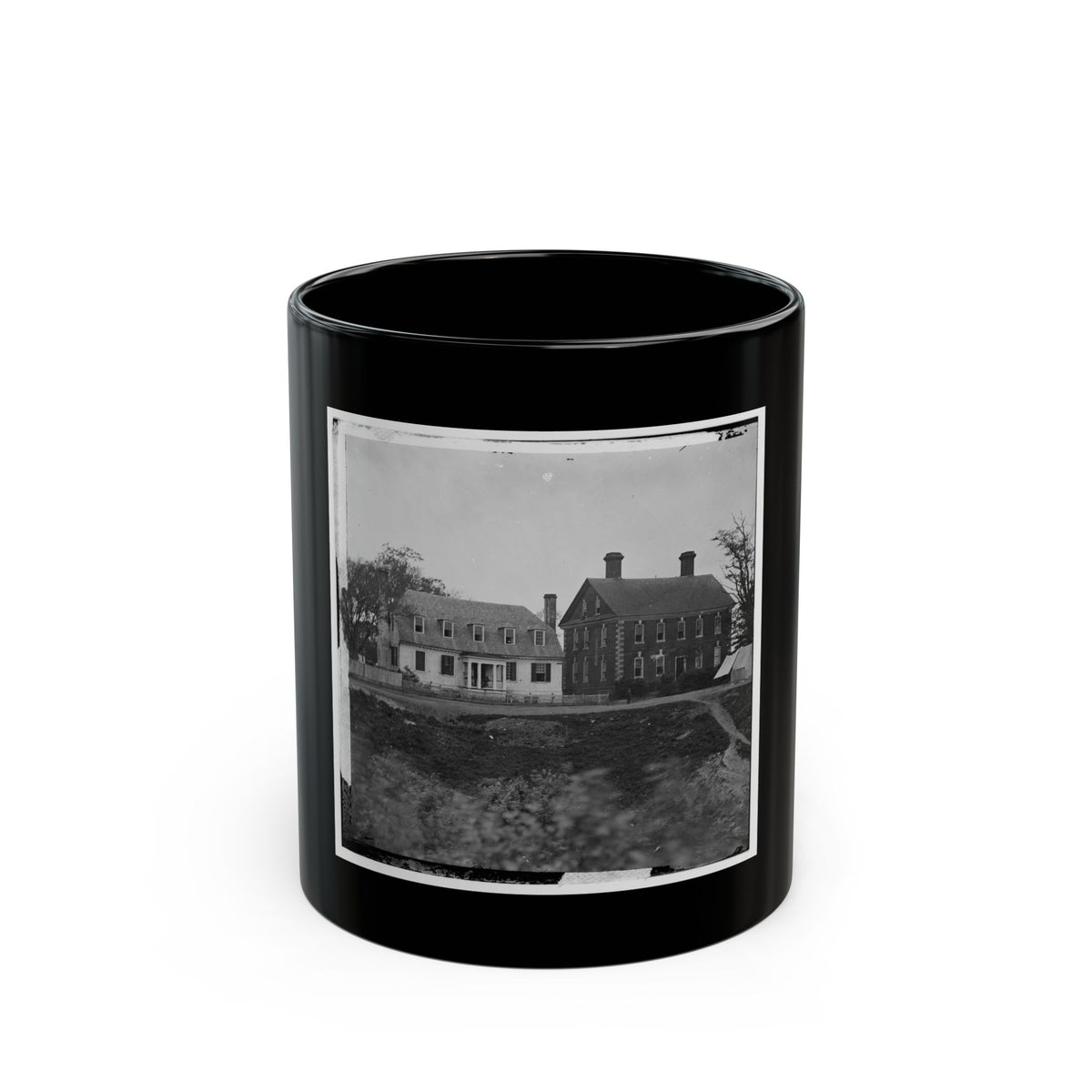 Black-and-white view of a two-storey brick house beside a white farmhouse, with a canvas tent by a dirt road.