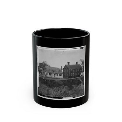 Black-and-white view of a two-storey brick house beside a white farmhouse, with a canvas tent by a dirt road.