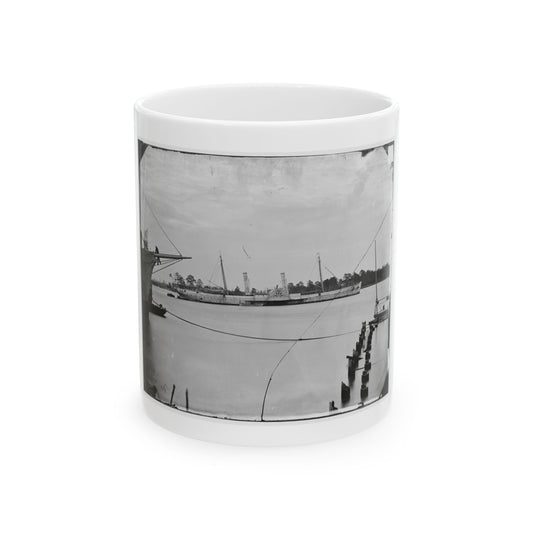 Black and white view of a paddle steamer with twin funnels on a calm river beside a warship bow.