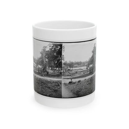 Black-and-white stereograph of a covered wagon by a riverbank among trees, with a seated figure in the grass in front.