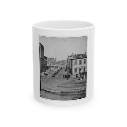 Black and white 1860s view of covered wagons on a city street lined with brick buildings and rail tracks.