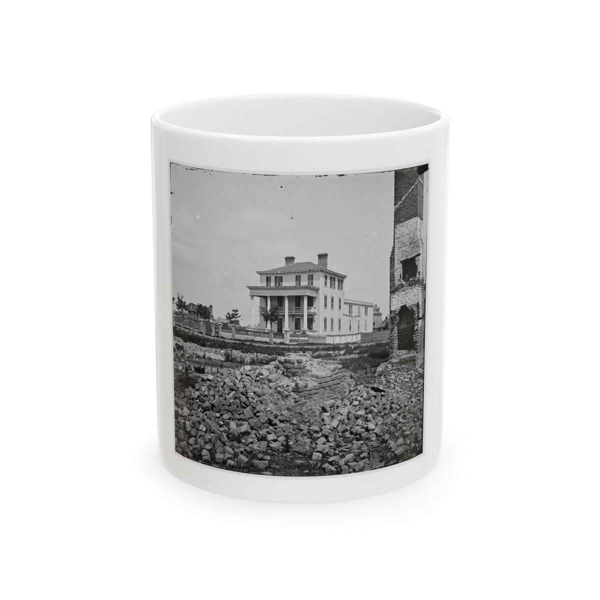 Black-and-white view of a columned wooden house beyond heaps of fallen bricks and a ruined brick chimney.