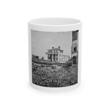 Black-and-white view of a columned wooden house beyond heaps of fallen bricks and a ruined brick chimney.