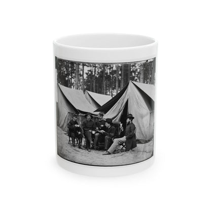 Black-and-white view of five men seated on folding chairs with cups before large canvas tents in a pine grove.