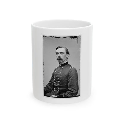 Black and white studio portrait of a waxed-mustached man in a double-breasted military frock coat on a grey backdrop.