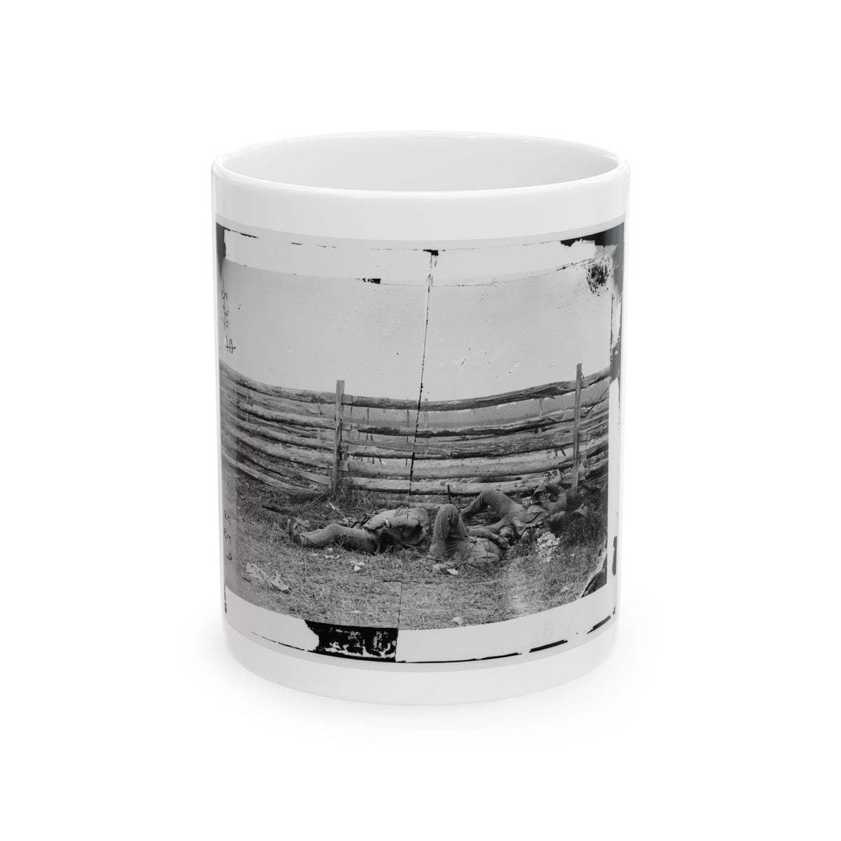 Black and white vintage view of three figures lying in grass beside a weathered split-rail fence.