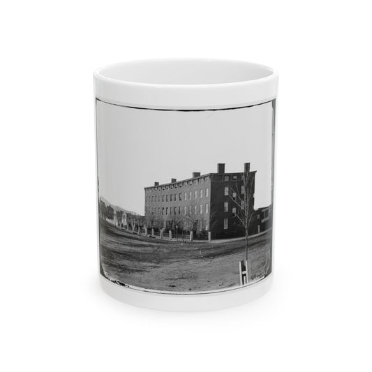 Black and white 1860s view of a four-storey brick building with rows of windows across an open dirt field.