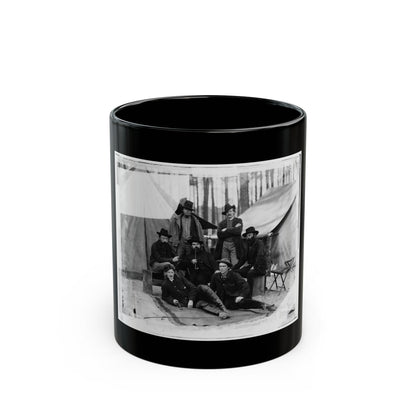 Black-and-white albumen view of seven men in coats, some smoking pipes, posed before canvas tents among pines.