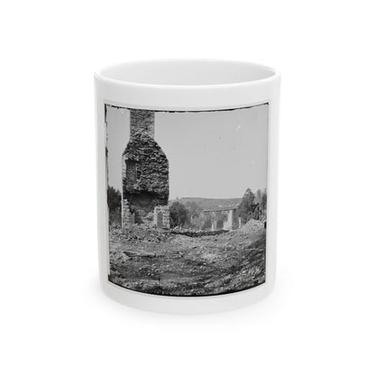 Black and white view of a ruined stone chimney rising above rubble, with a wooden trestle bridge beyond.