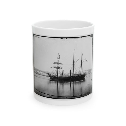 Black and white view of a three-masted paddle steamer with sailors on its rigging, moored on calm water.