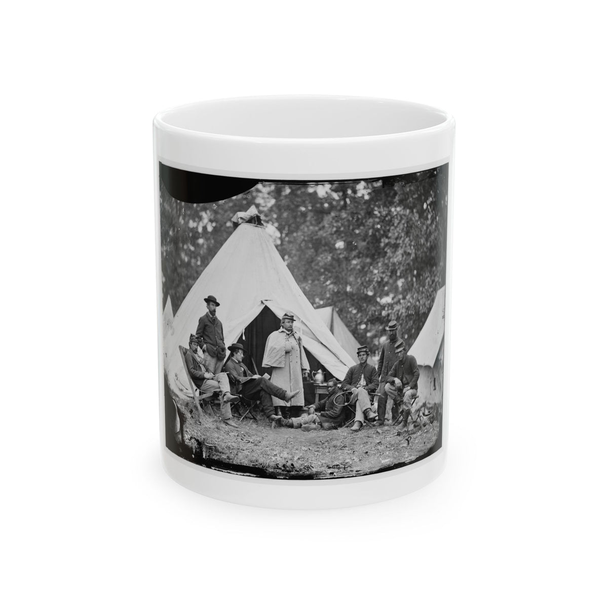 Black and white view of eight men gathered in a camp beside a large white conical tent under trees.