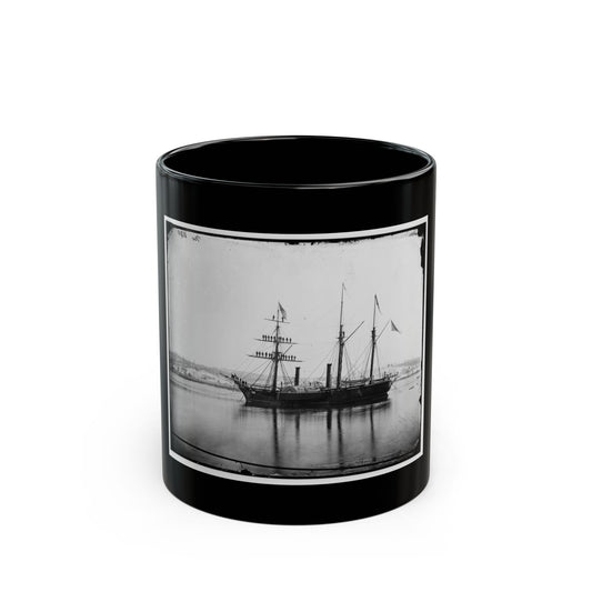 Black and white view of a three-masted paddle steamer with sailors on its rigging, moored on calm water.