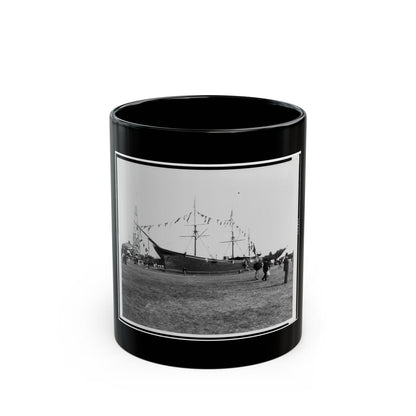 Black and white view of an old sailing ship on a grassy field, decorated with pennant flags and visitors nearby.