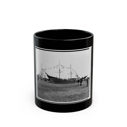 Black and white view of an old sailing ship on a grassy field, decorated with pennant flags and visitors nearby.