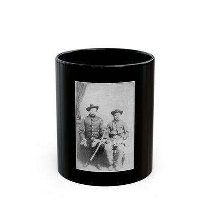 Black and white studio portrait of two seated men in wide-brimmed hats and military-style coats, one holding a sword.