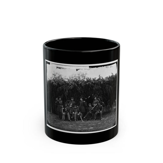 Black and white group portrait of seven uniformed officers, some holding sabres, before a dense drooping tree.