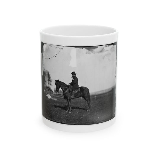 Black and white scene of a bearded rider in a hat and dark coat seated on a dark horse in an open field.