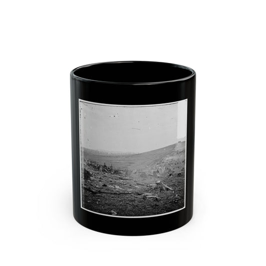 Grainy black and white print showing soldiers sheltered behind log breastworks in a cleared field with wooden huts.