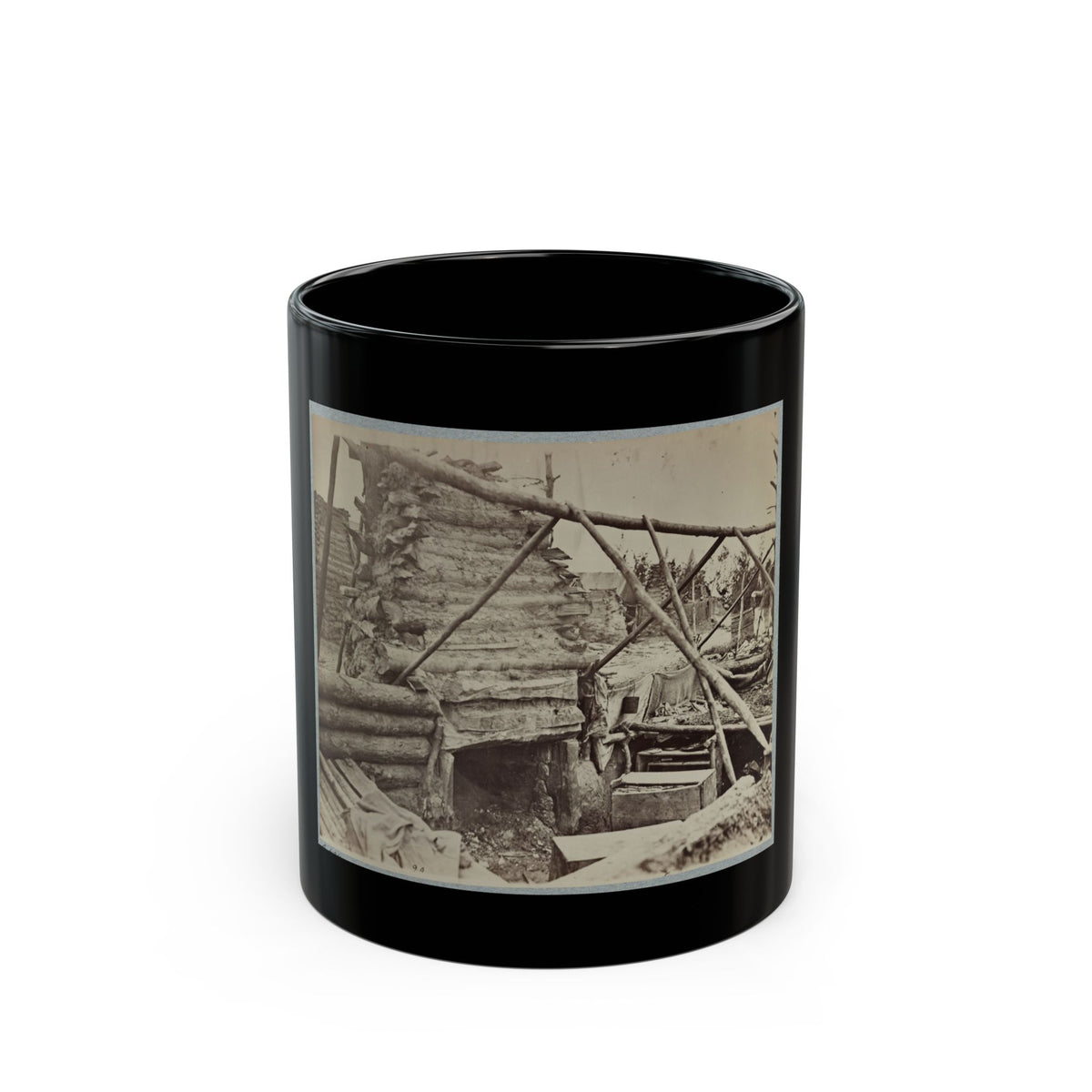 Sepia view of a rough log hut with a stone chimney base, braced by poles, beside wooden crates in camp.