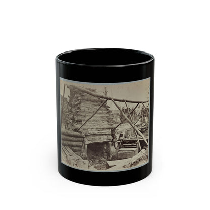 Sepia view of a rough log hut with a stone chimney base, braced by poles, beside wooden crates in camp.