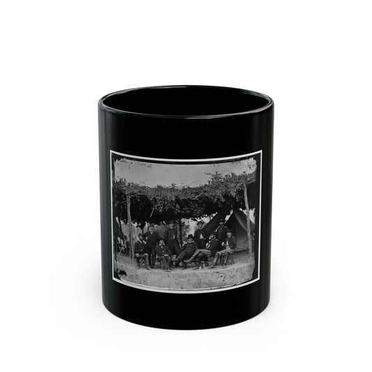 Black and white group portrait of nine uniformed officers beneath a leafy canopy in front of a canvas tent.