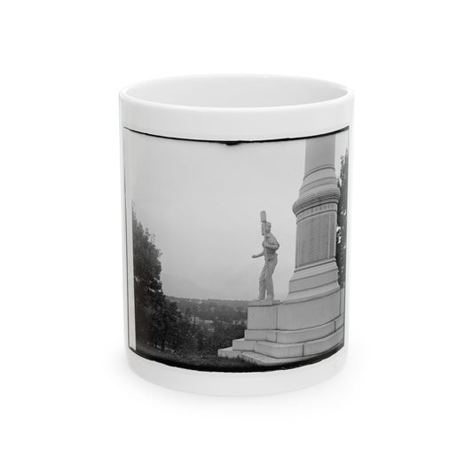 Black and white view of a stone soldier statue holding a rifle beside a tall monument column, valley beyond.