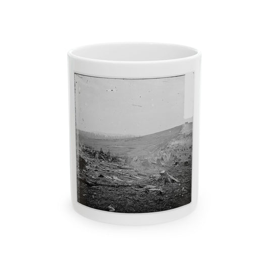 Grainy black and white print showing soldiers sheltered behind log breastworks in a cleared field with wooden huts.
