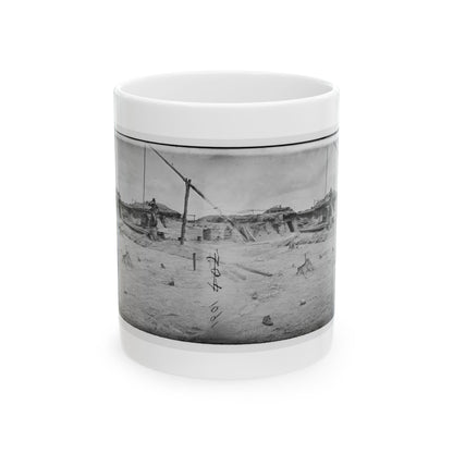 Black and white stereo view of a sandy military camp with earthen dugouts, barrels and a standing soldier.