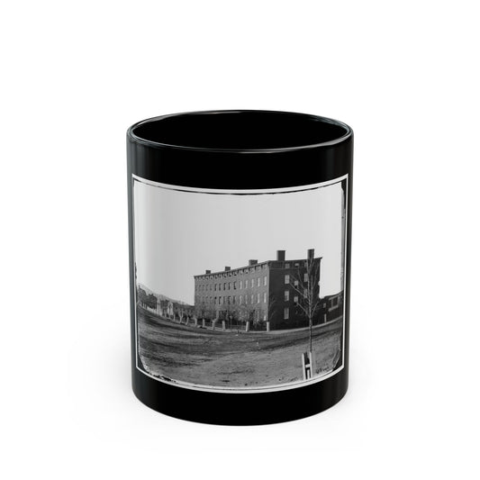 Black and white 1860s view of a four-storey brick building with rows of windows across an open dirt field.