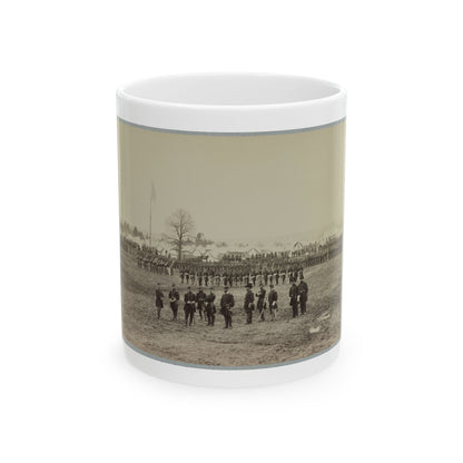 Sepia print showing officers on an open field before ranks of soldiers and rows of white tents, with a flag.
