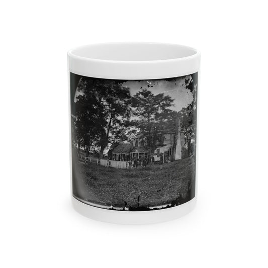 Black-and-white view of four men standing in a grassy field before a wooden farmhouse with a brick chimney.