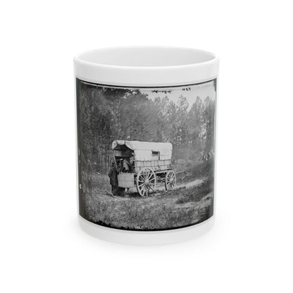 Black-and-white view of a canvas-covered supply wagon with spoked wheels on grass, a man in a long coat beside it.