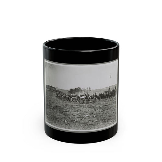 Black and white view of soldiers hauling field cannons across an open field, with mounted men and horses.