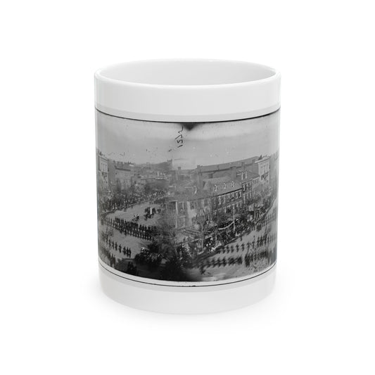 Black and white stereo view of troops marching in columns down a wide city avenue lined with townhouses and crowds.