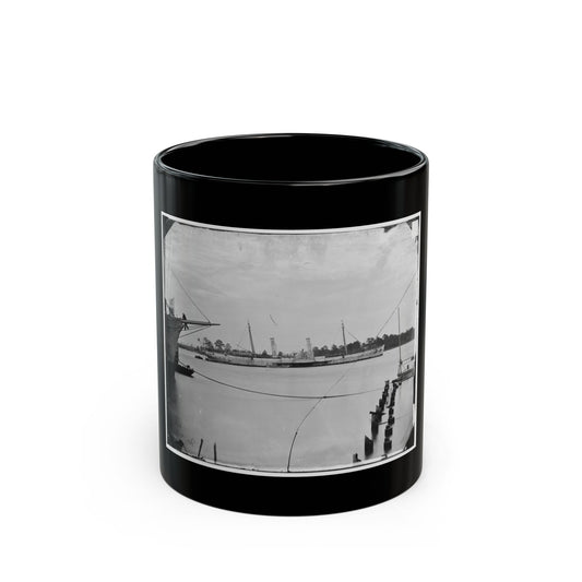 Black and white view of a paddle steamer with twin funnels on a calm river beside a warship bow.