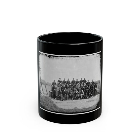 Black and white group portrait of about two dozen uniformed soldiers posed with swords on an earthwork.
