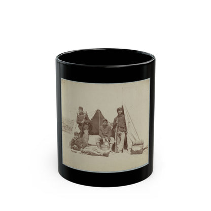 Sepia print showing five soldiers in kepi caps posed with rifles beside canvas tents and bedrolls in camp.