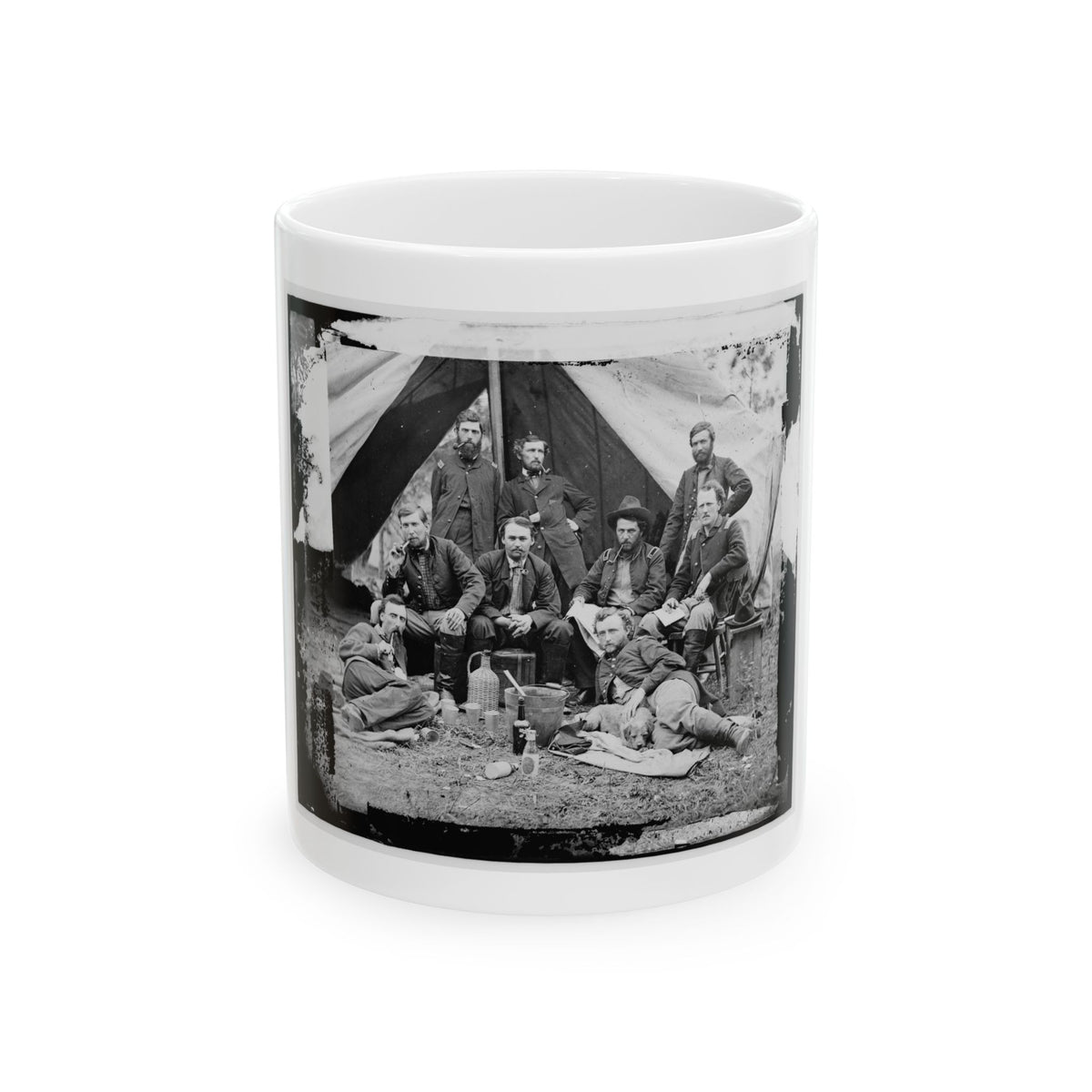 Black and white scene of eight men in military coats posed before a canvas tent, some smoking pipes.