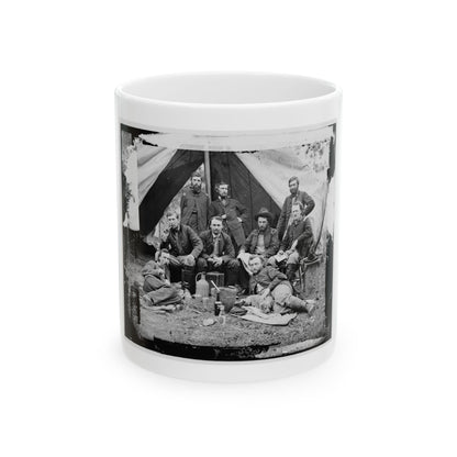 Black and white scene of eight men in military coats posed before a canvas tent, some smoking pipes.