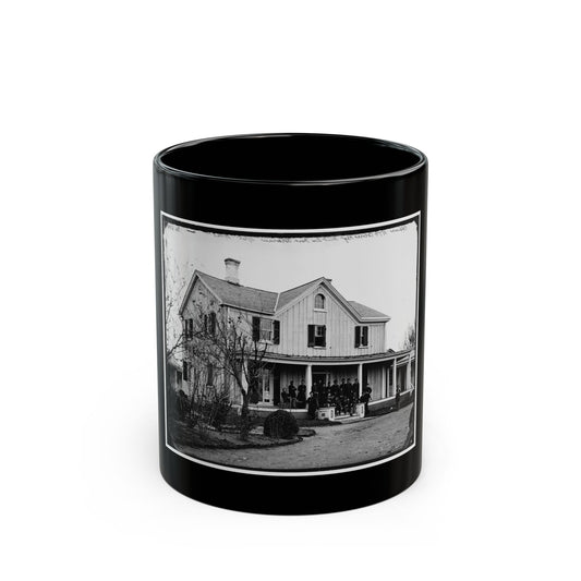 Black and white view of uniformed men posed on the porch of a two-story wooden house with bare trees.