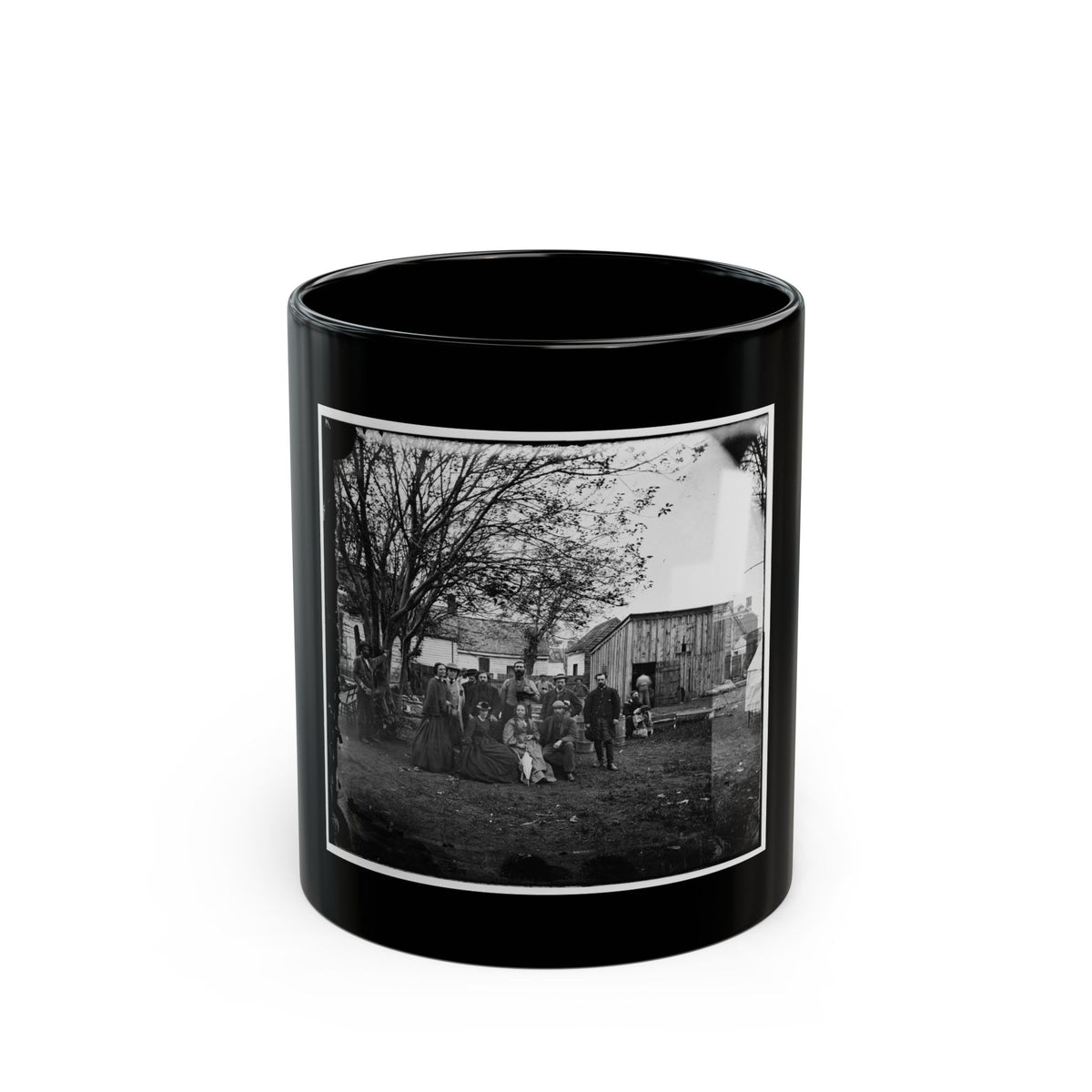Black and white 19th-century group scene of about a dozen people in a yard beside a plank shed and bare tree.