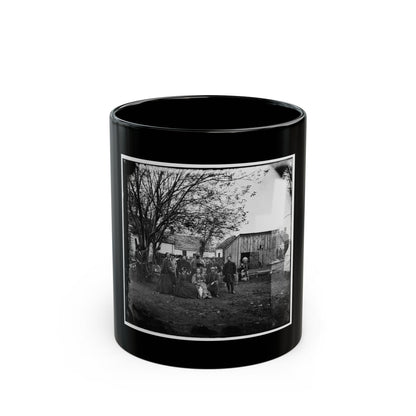 Black and white 19th-century group scene of about a dozen people in a yard beside a plank shed and bare tree.