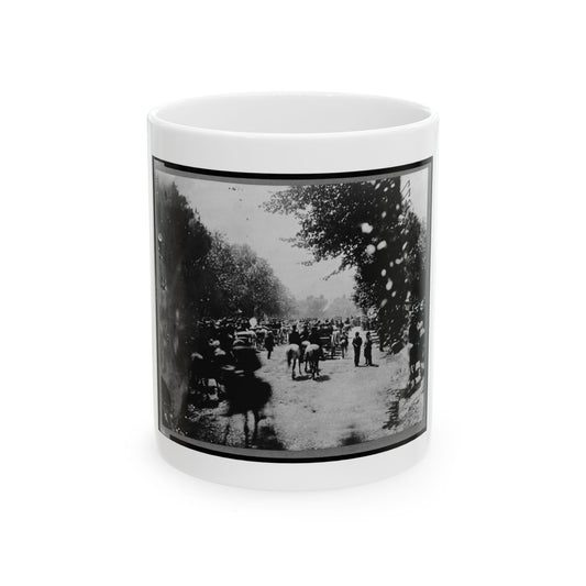 Black and white view of a blurred crowd of mounted riders and wagons on a tree-lined dirt road.