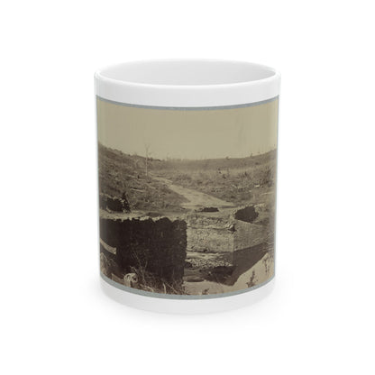 Sepia view of ruined stone bridge abutments over a creek, with a dirt road climbing a barren hillside.